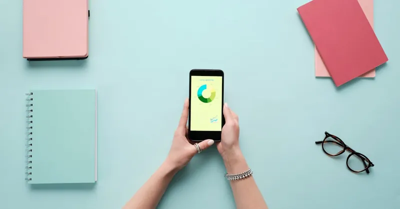 Overhead view of smartphone displaying business analytics on a vibrant blue background with stationery items.