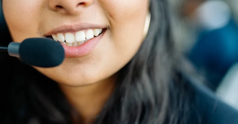 Close-up of a smiling customer service agent wearing a headset in an office environment.