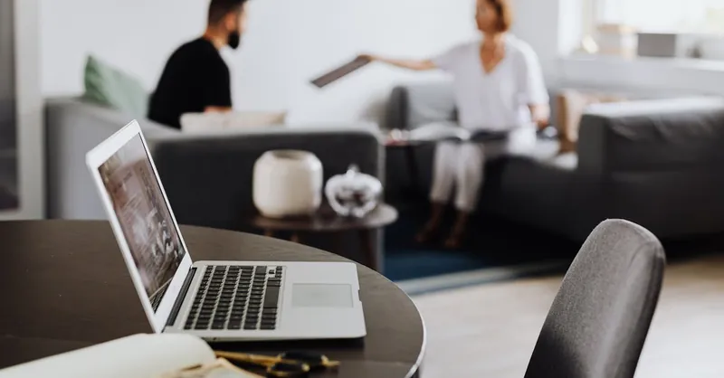 Modern workspace featuring a laptop on a table with blurred figures in the background.