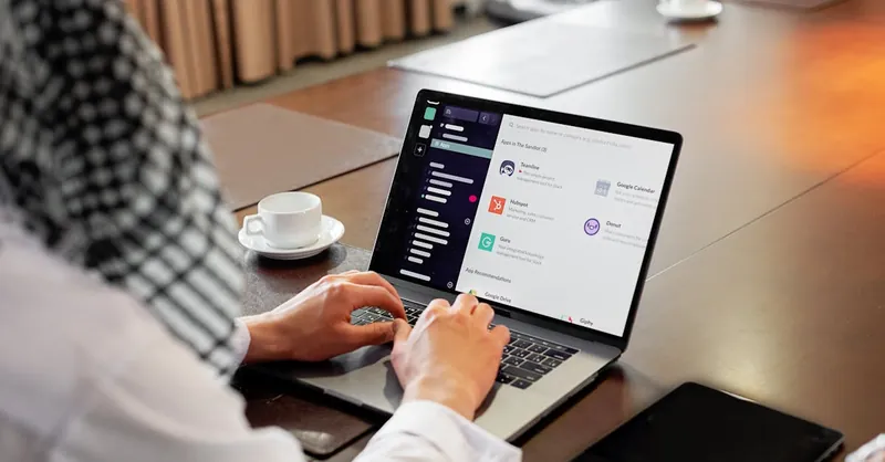 Businessman using messaging app on laptop in modern office, engaging in team collaboration.