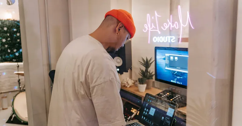 Man working on music production in a modern studio with laptop and equipment.