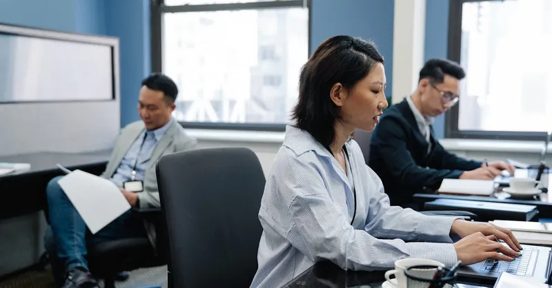 Focused Asian professionals working on laptops in a modern office environment, emphasizing collaboration.