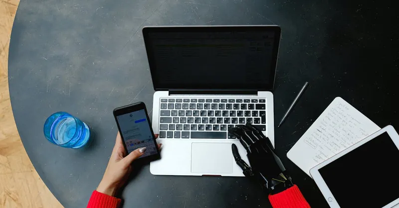 A person using a laptop, smartphone, and tablet with a prosthetic hand, emphasizing digital connectivity.