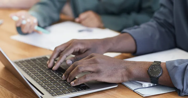 Close-up of hands typing on a laptop, with a focus on modern office tools and teamwork.