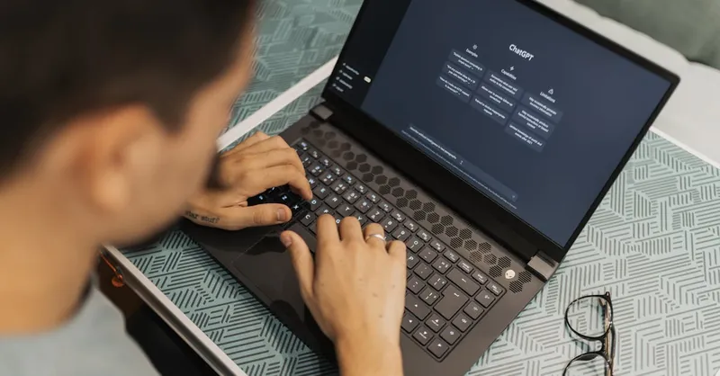 A man working on a laptop with AI software open on the screen, wearing eyeglasses.