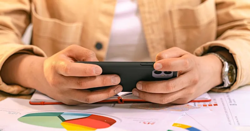 A business professional using a smartphone to analyze charts and graphs, likely for work.