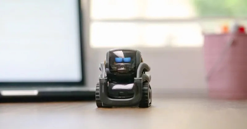 Small toy robot on a desk beside a laptop, symbolizing technology and innovation.