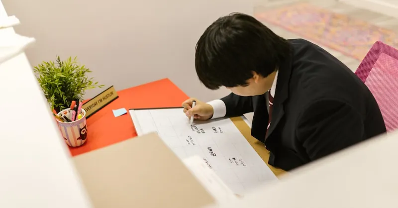 Business professional writing on monthly calendar at desk in modern office.