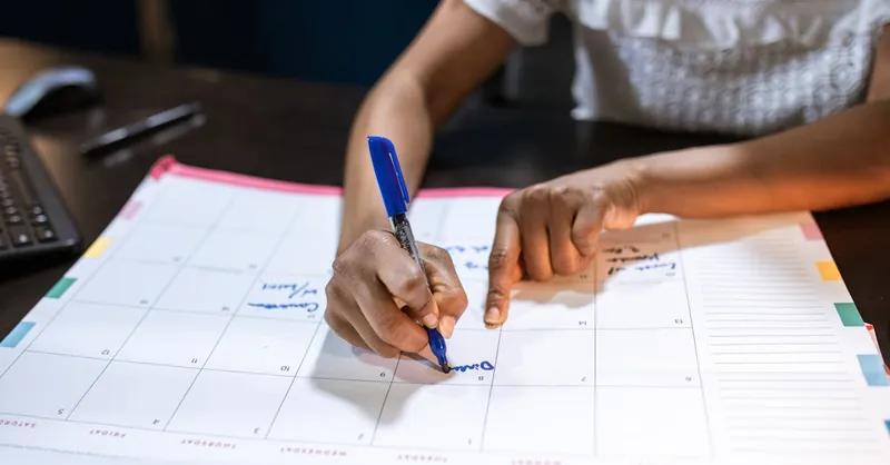 A woman marks important dates on her desk calendar, planning upcoming events.