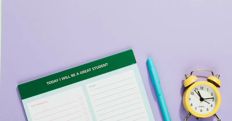 A vibrant still life with a motivational student planner, pen, and yellow alarm clock on a pastel backdrop.