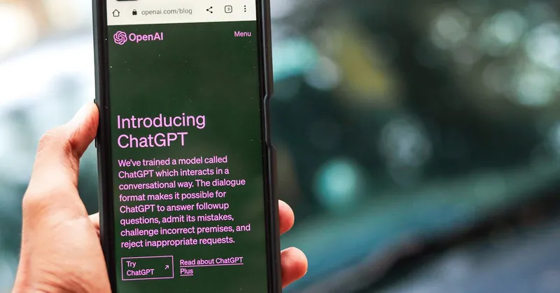 Close-up of a smartphone showing ChatGPT details on the OpenAI website, held by a person.