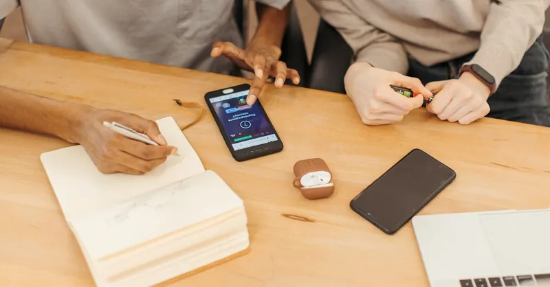 Teamwork at a table using smartphones, notebooks, and laptops to collaborate in an office setting.