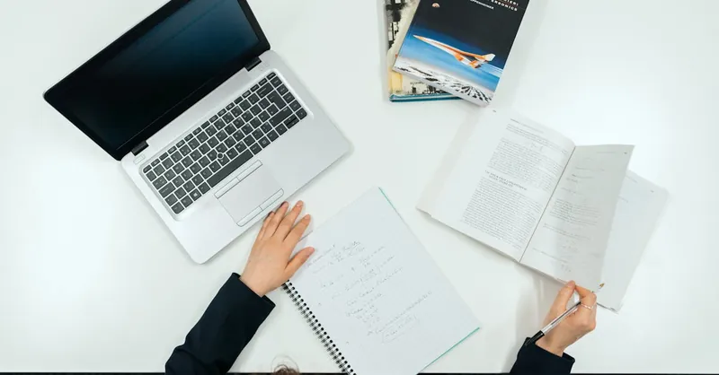 Top view of a work desk with laptop, books, and notes showcasing productivity.