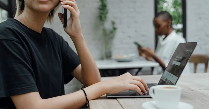 People working remotely in a modern café, using laptops and phones for business tasks.