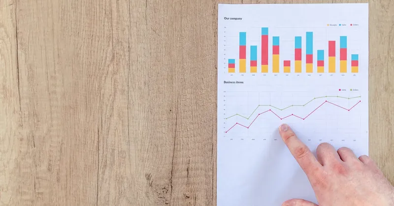 Hand analyzing business graphs on a wooden desk, focusing on data results and growth analysis.