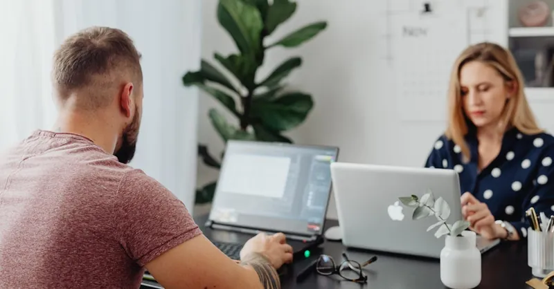 Two coworkers using laptops in a modern office setting, focusing on collaborative work.