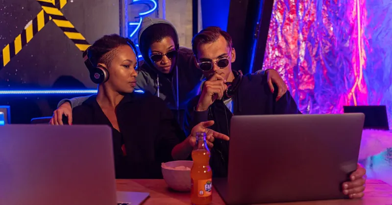 Three people collaborate on laptops in a cyber-themed workspace, discussing strategies.