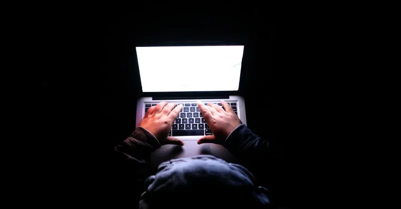 A person in a dark room typing on a laptop, symbolizing privacy, cybersecurity, and technology.