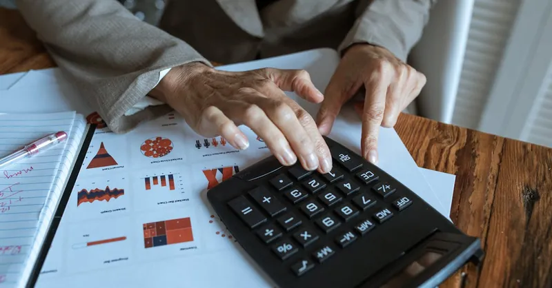 A businessman using a calculator to analyze financial charts and graphs on a desk.