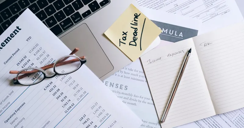 Workspace with laptop, documents, and tax deadline note for financial management.