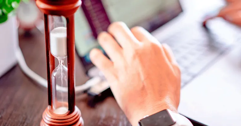 Close-up of a hand on a laptop with an hourglass, symbolizing time management and productivity.