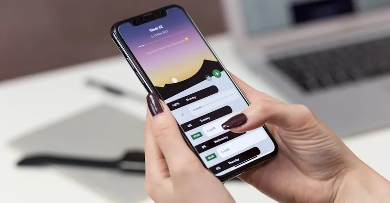 A woman interacts with a productivity app on her smartphone at a desk setup.