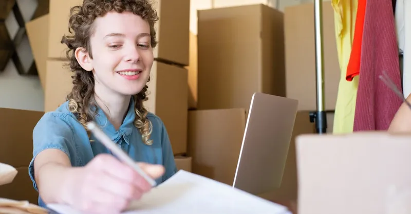 Smiling young woman managing a small business with laptop and packages around her.