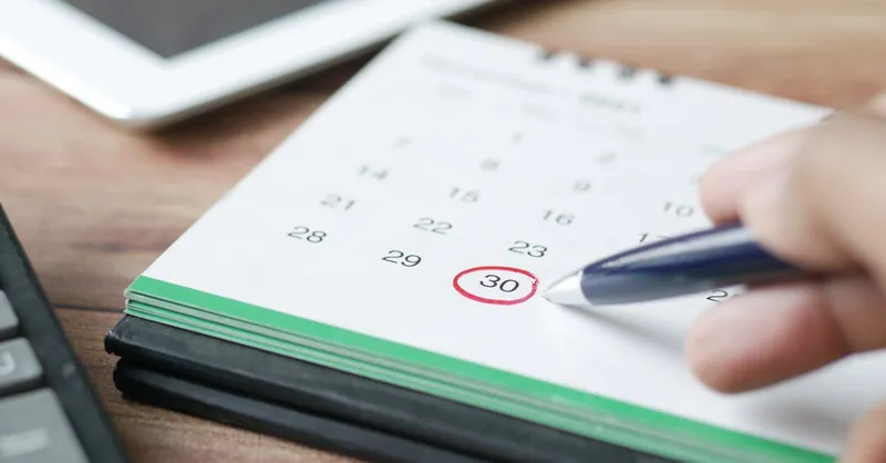 Close-up shot of a hand marking a date on a calendar with a pen, emphasizing planning and scheduling.